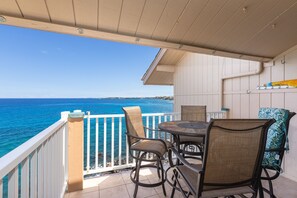 A balcony with a view of the ocean, a table with chairs, and a white railing. - Sea Village 4313 2 Bedroom Condo (Kailua-Kona)