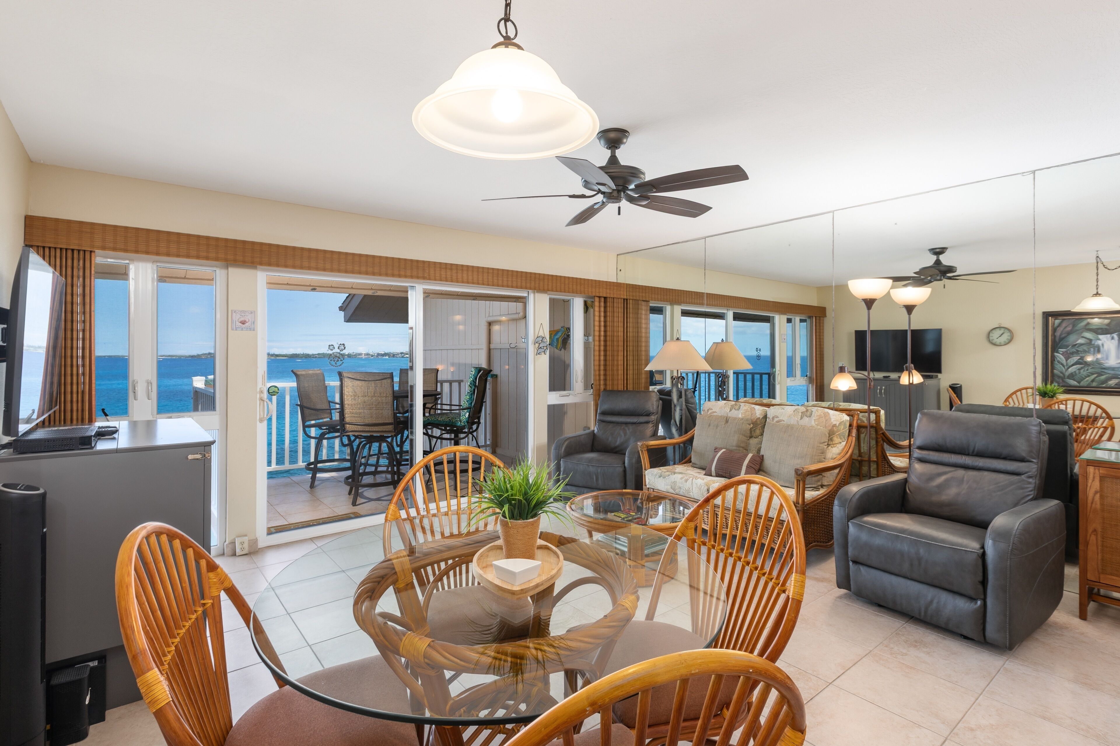 A spacious living area with a glass table, wicker chairs, a leather sofa, and a ceiling fan.