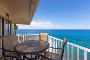 A balcony with a round table and chairs, overlooking a clear blue ocean with a white railing. - Sea Village 4313 2 Bedroom Condo (Kailua-Kona)