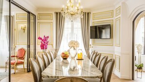 Une salle à manger avec une table en marbre, des murs ornés de motifs dorés et un lustre.