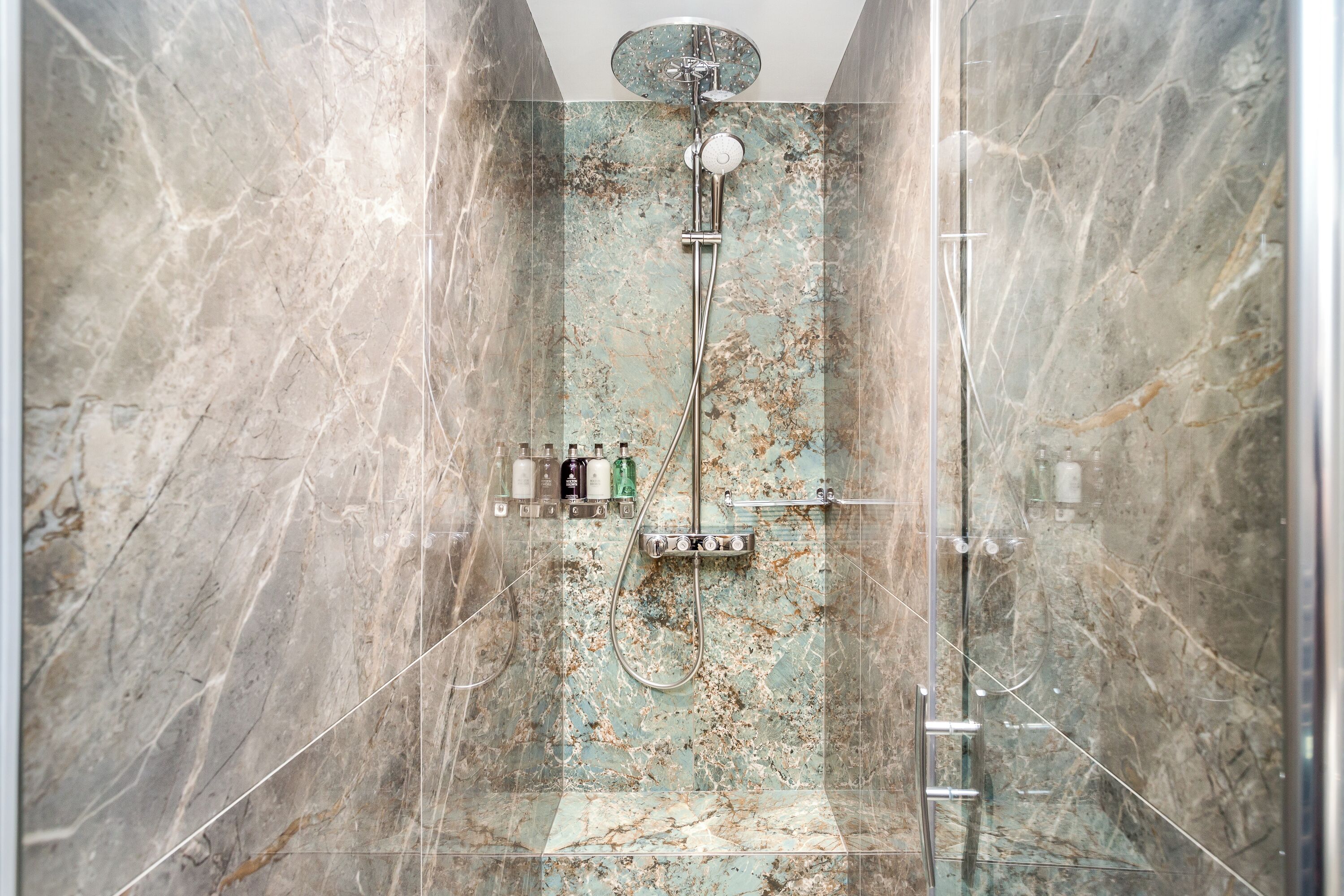 Een douche met glazen wanden, een marmeren wand, een handdouche en een wandmengkraan.