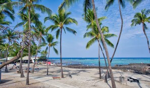 A beach with palm trees, a rocky shoreline, and a clear blue sky. - Country Club Villas #216 2 Bedroom Condo (Kailua-Kona)