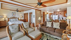 Ein geräumiger Wohnbereich mit Deckenventilator, Korbmöbeln, einem braunen Sofa und einer Küche im Hintergrund.