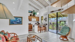A spacious living area with a sofa, wicker chairs, a glass coffee table, and a kitchen in the background. - Kona Makai 3305 2 Bedroom Condo (Kailua-Kona)