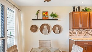 Un'area pranzo con mobili in vimini, una mensola a parete con oggetti decorativi e una cucina con pensili in legno.