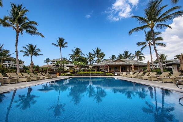 A swimming pool with lounge chairs and palm trees, surrounded by resort buildings.