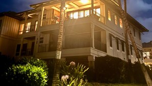 A two-story house with a balcony, surrounded by palm trees, under a twilight sky.