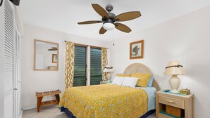 A bedroom with a bed, bedside table, lamp, and a ceiling fan. - Sea Village 4113 2 Bedroom Condo (Kailua-Kona)