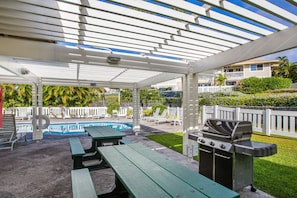 Un espacio al aire libre techado con piscina, mesas de picnic y una parrilla.