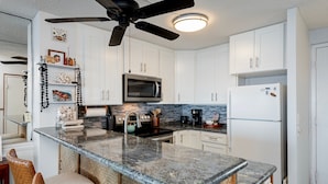 A kitchen with white cabinets, a black ceiling fan, a microwave, and a refrigerator. - Alii Villas #232 2 Bedroom Condo (Kailua-Kona)
