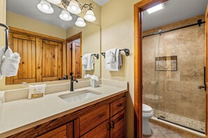 Un baño con tocador de madera, lavamanos, espejo y cabina de ducha de vidrio.