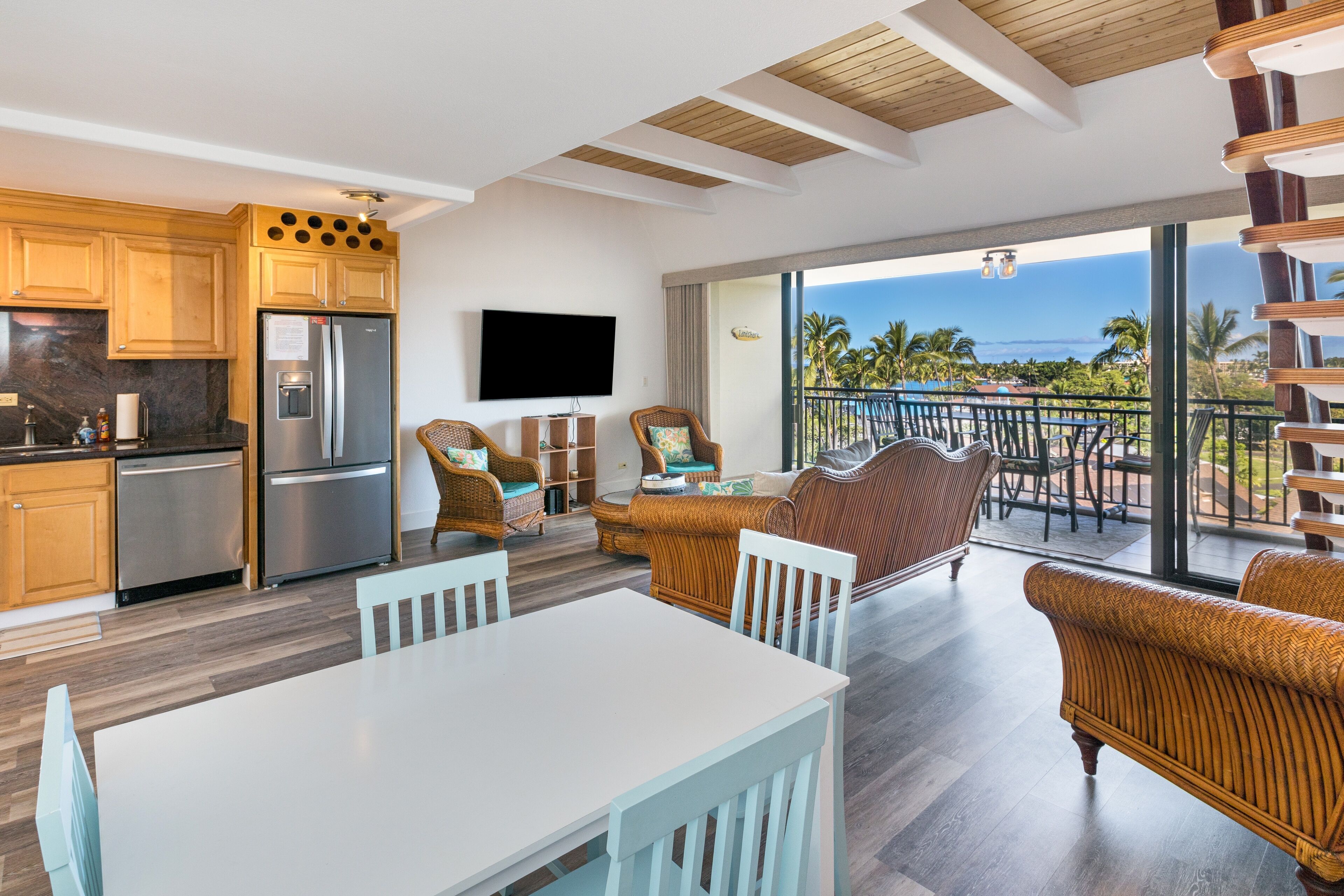 A modern kitchen with stainless steel appliances, a dining area with wicker furniture, and a balcony with a view of the ocean.