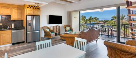 A modern kitchen with stainless steel appliances, a dining area with wicker furniture, and a balcony with a view of the ocean.