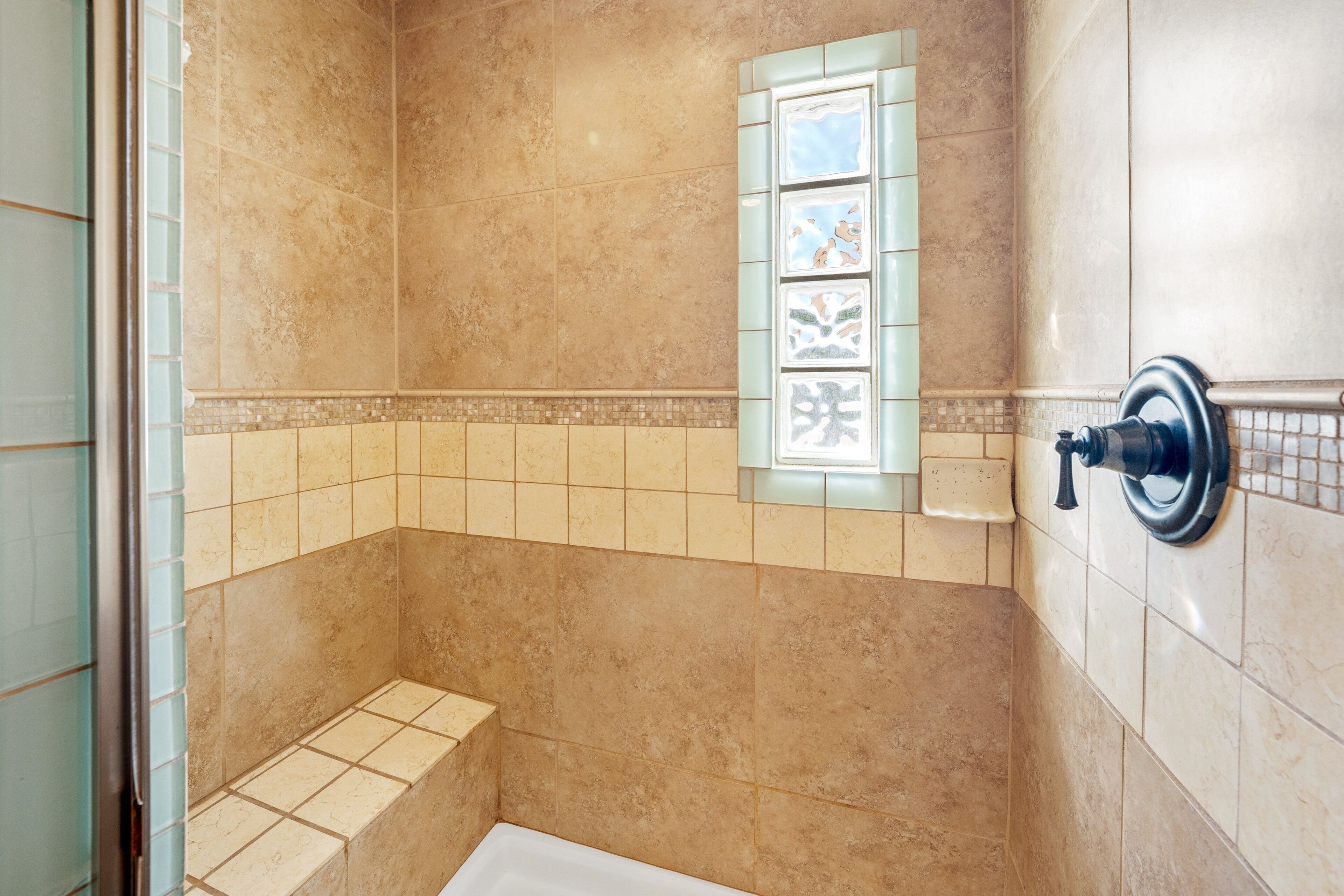 Casa de banho com azulejos bege, janela com azulejos decorativos e zona de duche.