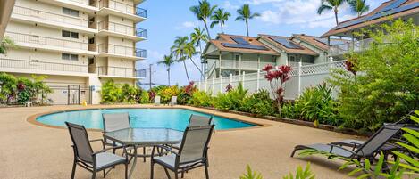A hotel with a swimming pool, outdoor seating, and palm trees.