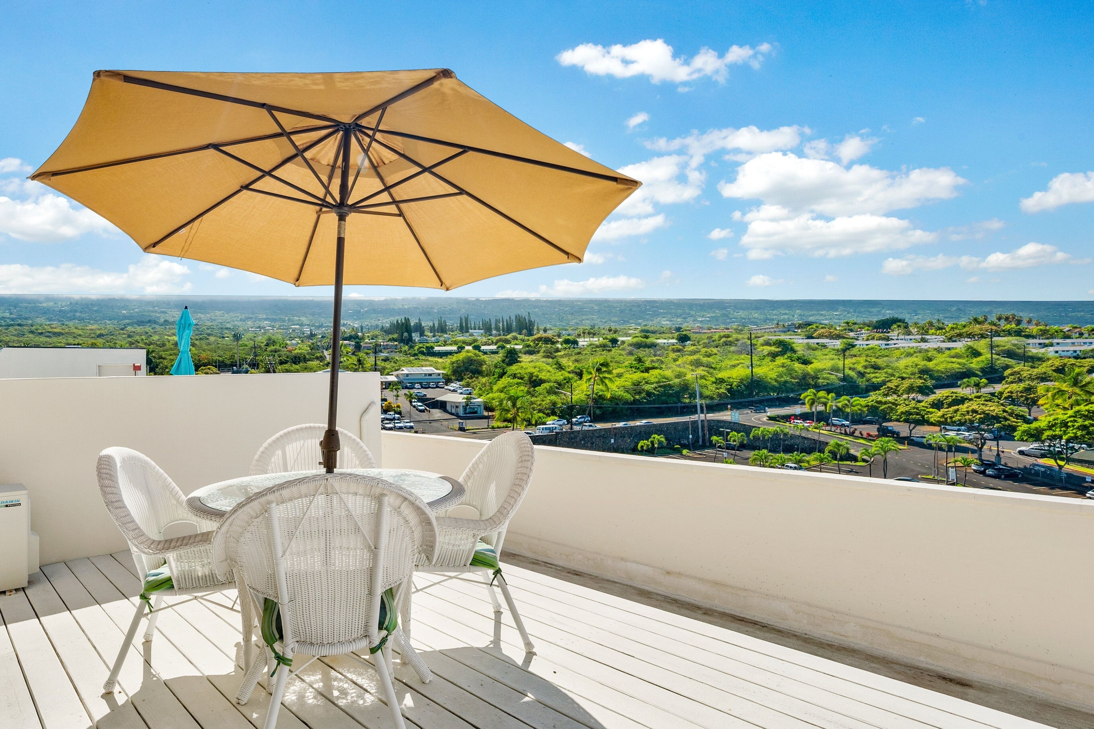 A balcony with a table and chairs, a yellow umbrella, and a view of a cityscape.