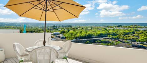 A balcony with a table and chairs, a yellow umbrella, and a view of a cityscape.