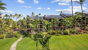 A hotel with multiple floors, a central courtyard with palm trees, and a clear blue sky. - Kona Makai 3301 2 Bedroom Condo (Kailua-Kona)
