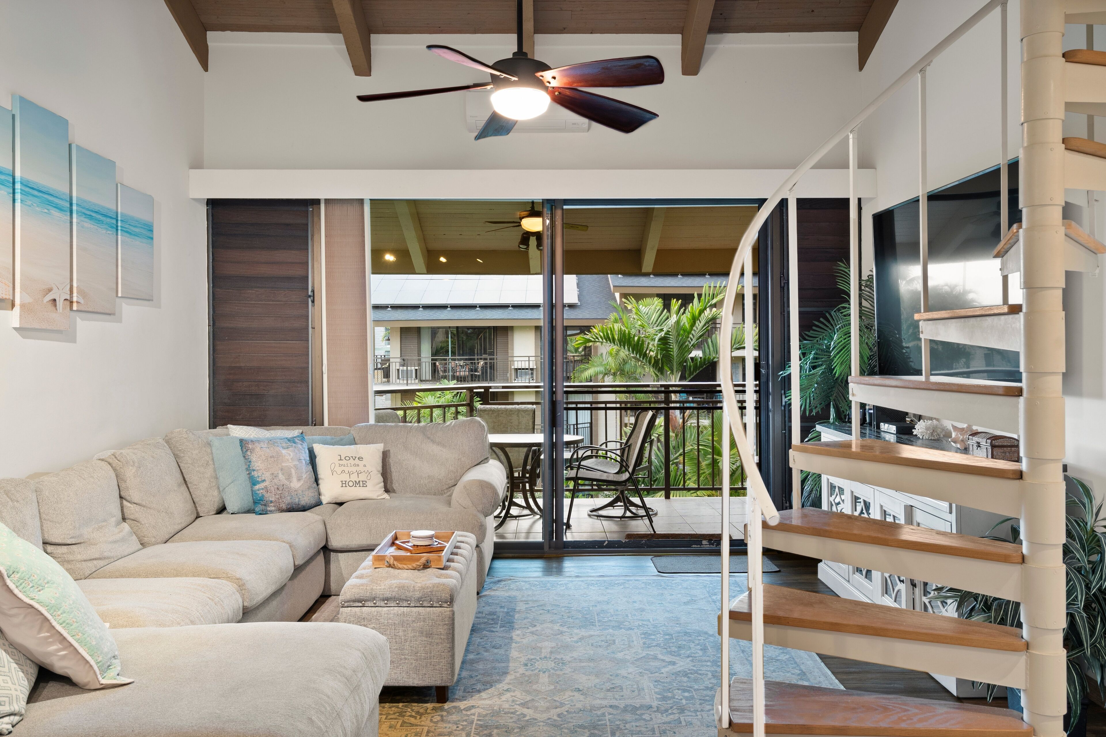 A modern living room with a sectional sofa, a ceiling fan, and a staircase leading to an upper level.