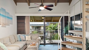 A modern living room with a sectional sofa, a ceiling fan, and a staircase leading to an upper level. - Kona Makai 3301 2 Bedroom Condo (Kailua-Kona)