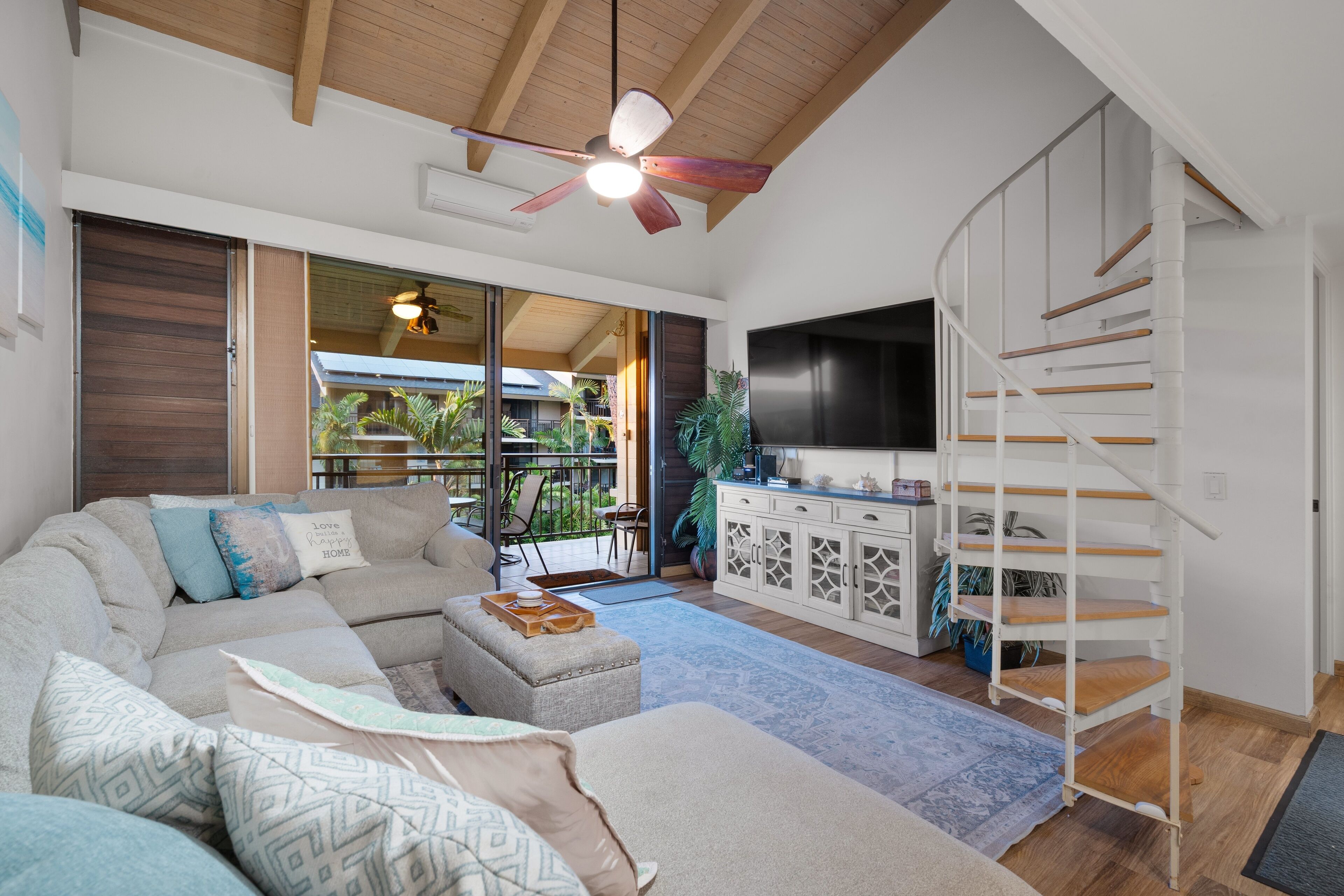 A modern living room with a sectional sofa, a flat-screen TV, and a staircase.