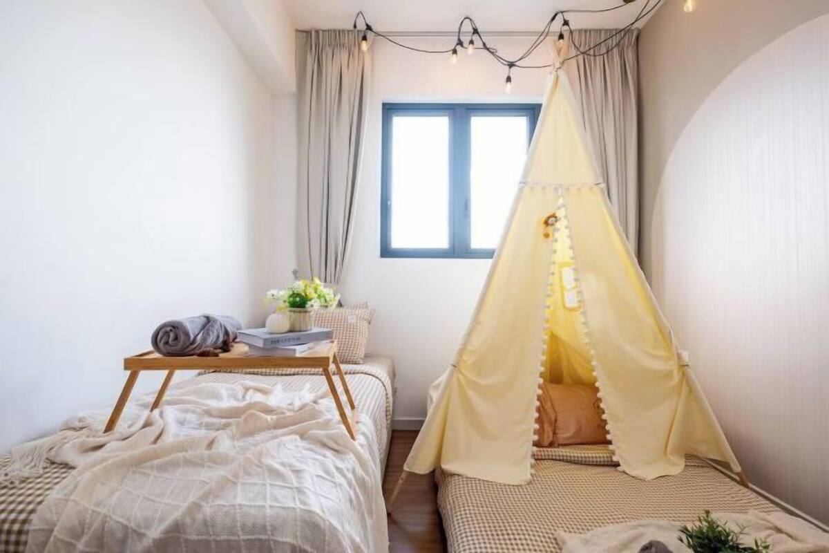 A bedroom with two beds, a bedside table with a lamp, and a window with curtains.