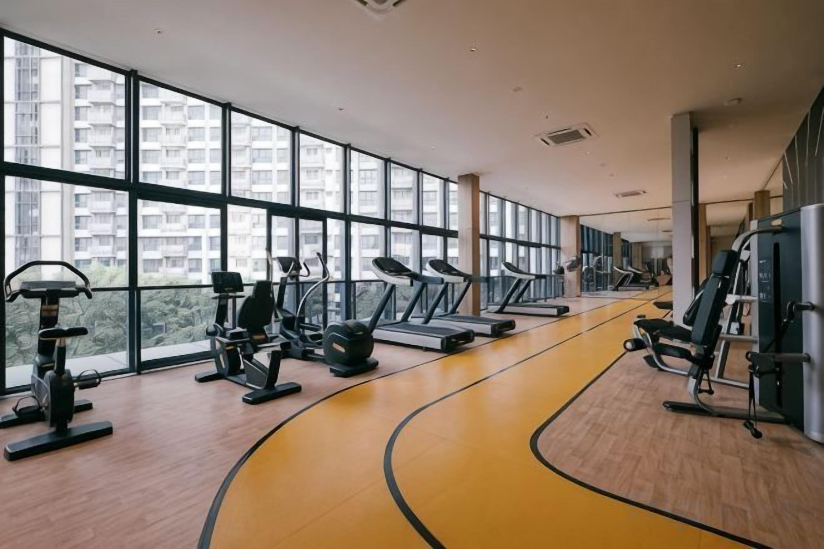 Une salle de sport équipée de machines de cardio, de postes d’entraînement avec poids et d’une piste de course jaune.