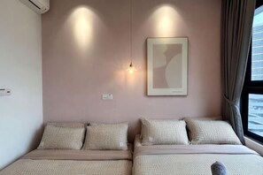 A bedroom with two beds, a wall-mounted light, and a window with curtains.