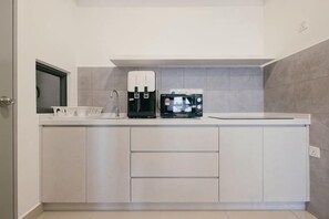 Una cocina moderna con cafetera integrada, microondas y lavamanos.