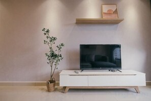 A modern living room with a flat-screen TV on a white cabinet, a small plant, and a shelf with a picture. - M Vertica Tower A Tower A by FEEL HOME (Kuala Lumpur)