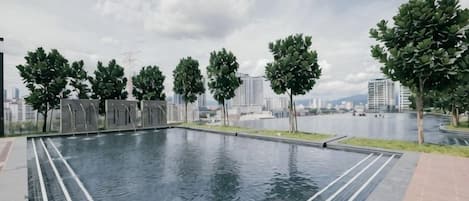 A swimming pool with a tiled border, surrounded by trees and a cityscape in the background.