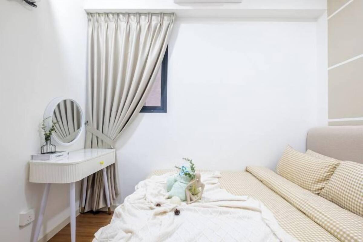 A bedroom with a bed, a bedside table with a mirror, and a window with curtains.