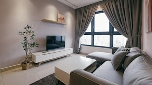 A modern living room with a flat-screen TV, a sofa, a coffee table, a plant, and a window with curtains. - M Vertica Tower A Tower A by FEEL HOME (Kuala Lumpur)