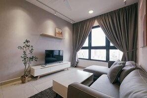Una sala de estar moderna con una televisión de pantalla plana, un sofá, una mesa de centro, una planta y una ventana con cortinas.
