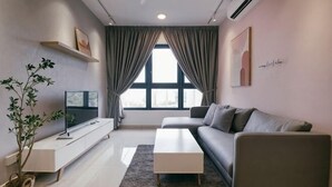 A modern living room with a sofa, a coffee table, a TV on a stand, a potted plant, and a large window with curtains. - M Vertica Tower A Tower A by FEEL HOME (Kuala Lumpur)