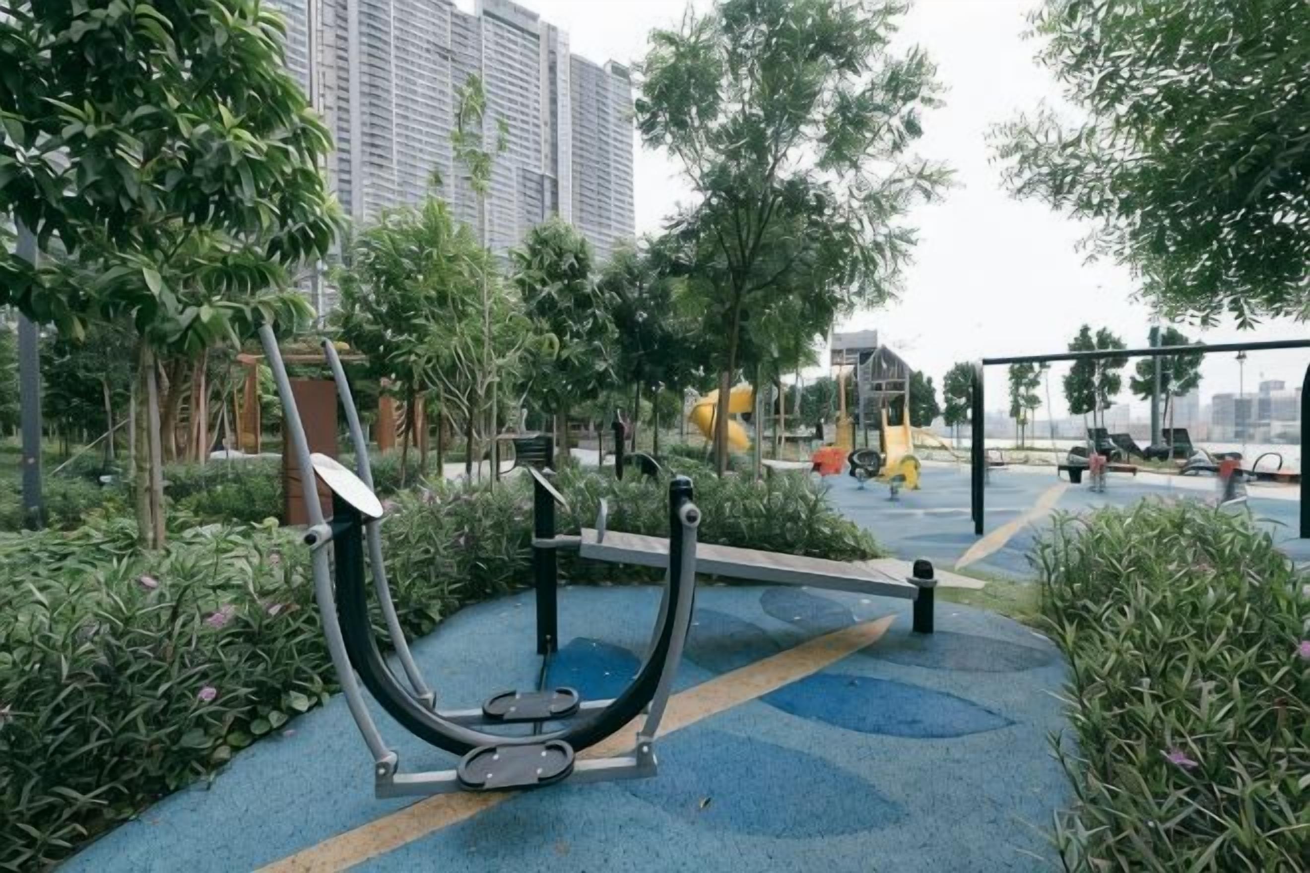 Zona de ejercicio al aire libre con bicicleta estática y máquina elíptica, rodeada de vegetación y un sendero pavimentado.