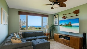 A living room with a sectional sofa, ottoman, wooden entertainment unit, and a large flat-screen TV. - Na Hale O Keauhou A4 3 Bedroom Condo (Kailua-Kona)