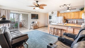 A modern kitchen with wooden cabinets, a central island, and a dining area with a table and chairs. - Alii Villas #301 1 Bedroom Condo (Kailua-Kona)