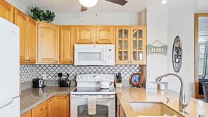 A kitchen with wooden cabinets, a white microwave, a stove, and a granite countertop. - Alii Villas #301 1 Bedroom Condo (Kailua-Kona)