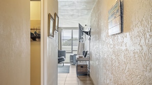 A hallway with a view of a room with a desk, chair, and a window with blinds. - Alii Villas #301 1 Bedroom Condo (Kailua-Kona)