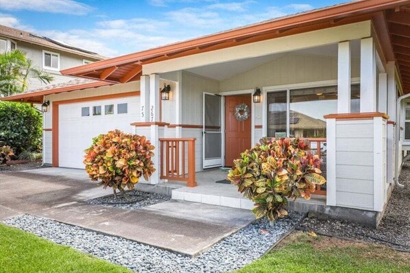 Une maison d’habitation avec un garage, une véranda dotée d’une balustrade et deux grands arbustes devant.