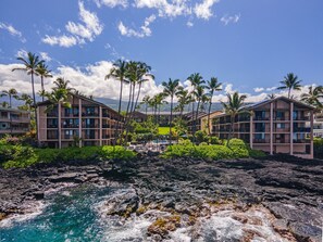 Ein Strandhotel mit mehreren Etagen, Palmen und einer felsigen Küstenlinie.