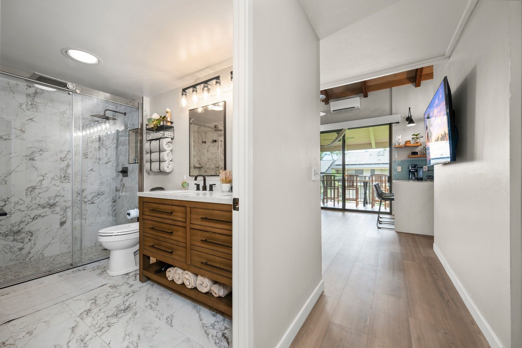 A modern bathroom with a glass shower, marble flooring, wooden vanity, and a large mirror.