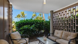 A patio with a sofa, chairs, and a table. There is a wooden fence and greenery in the background.
