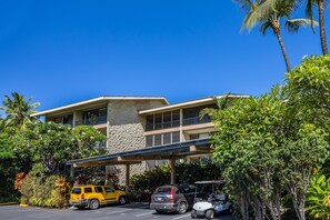 Ein Hotel mit überdachtem Parkbereich, mehreren Fahrzeugen und üppiger Bepflanzung.