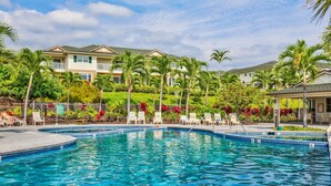 A swimming pool with lounge chairs, palm trees, and a building with a green roof in the background. - Na Hale O Keauhou G4 3 Bedroom Condo (Kailua-Kona)