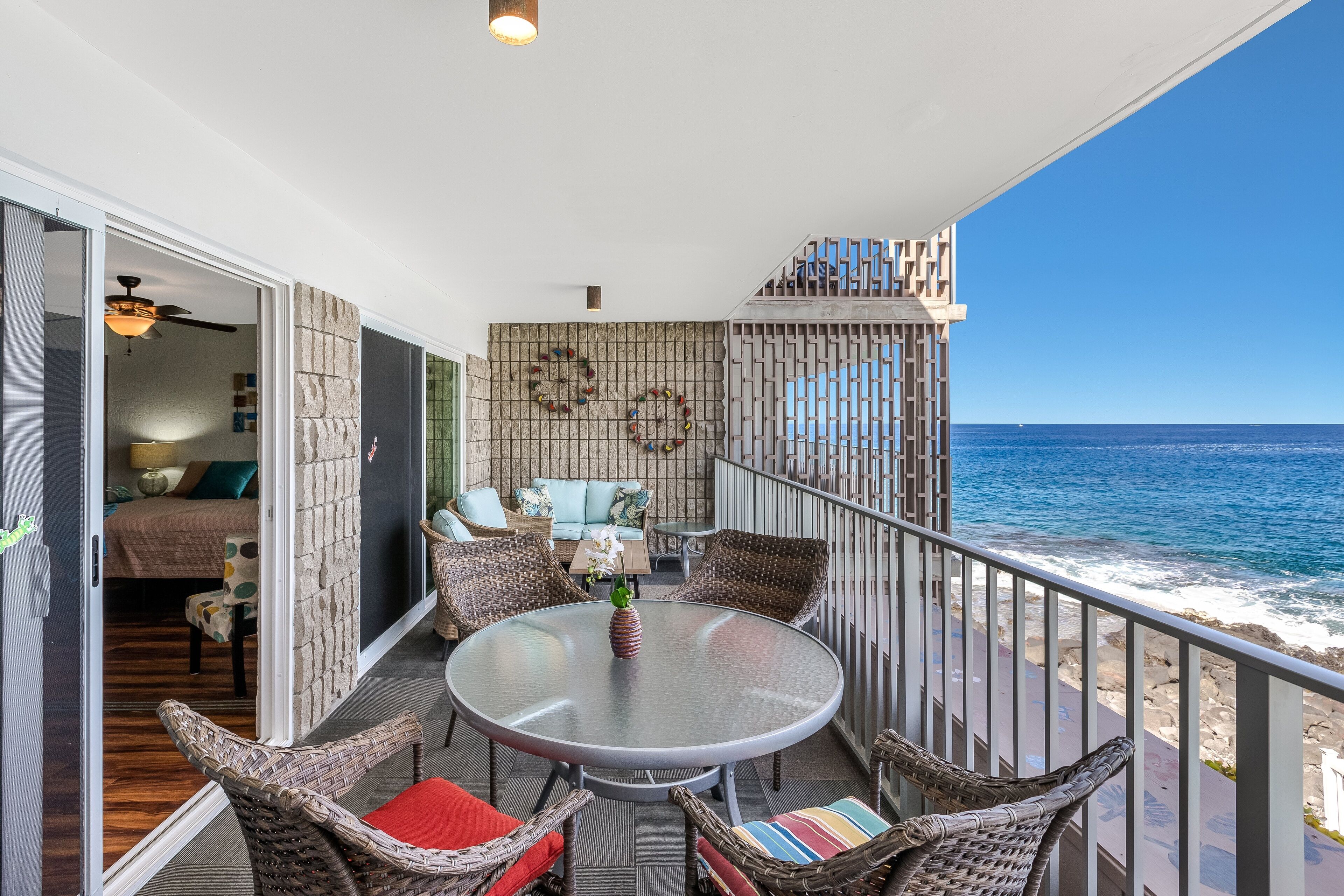 A balcony with wicker furniture, a glass table, and a view of the ocean.