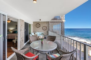 A balcony with wicker furniture, a glass table, and a view of the ocean. - Alii Villas #230 2 Bedroom Condo (Kailua-Kona)