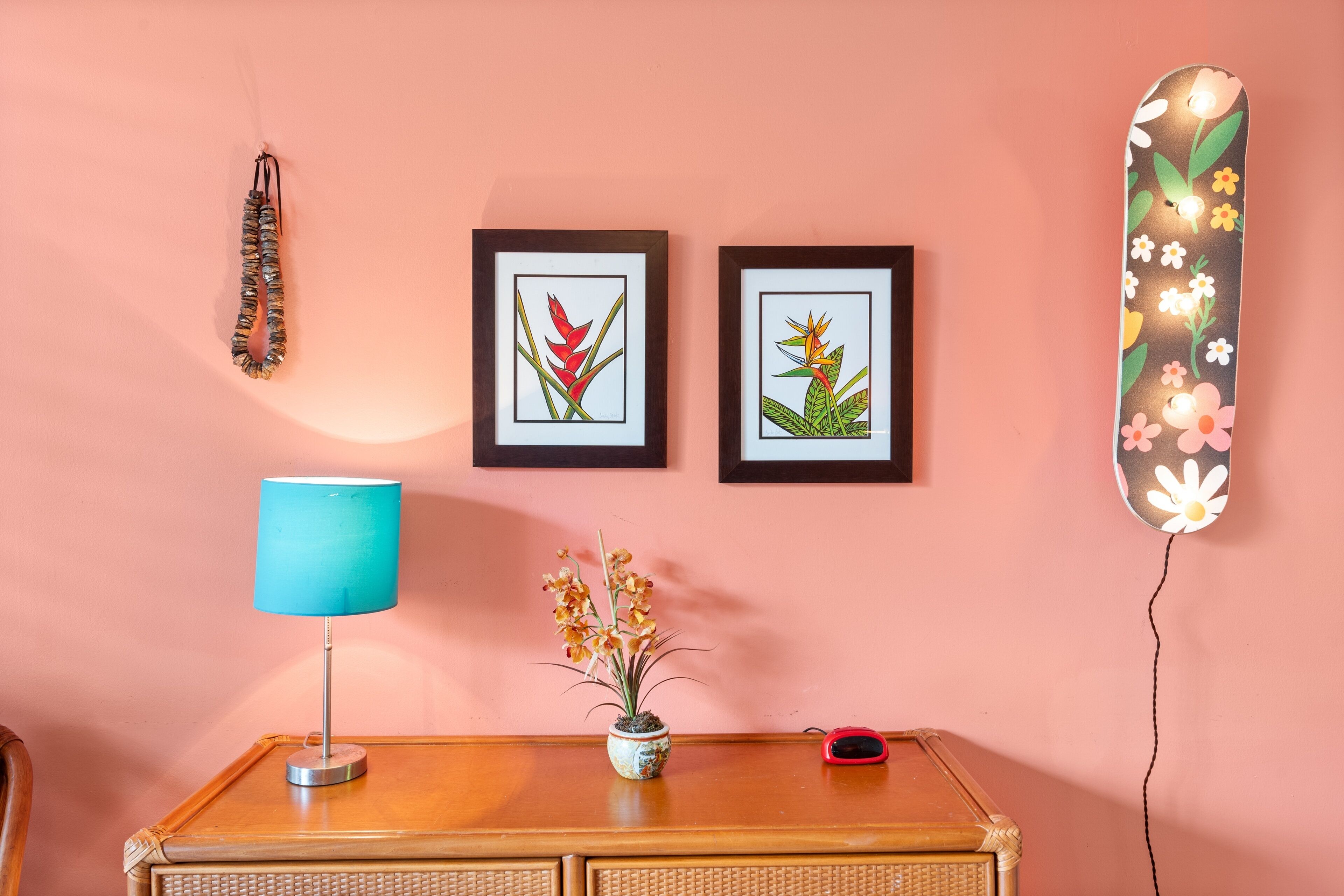 Ein Zimmer mit einem Holztisch, einer blauen Lampe, einem kleinen Topfpflanzen und zwei gerahmten Pflanzenabbildungen an der Wand.