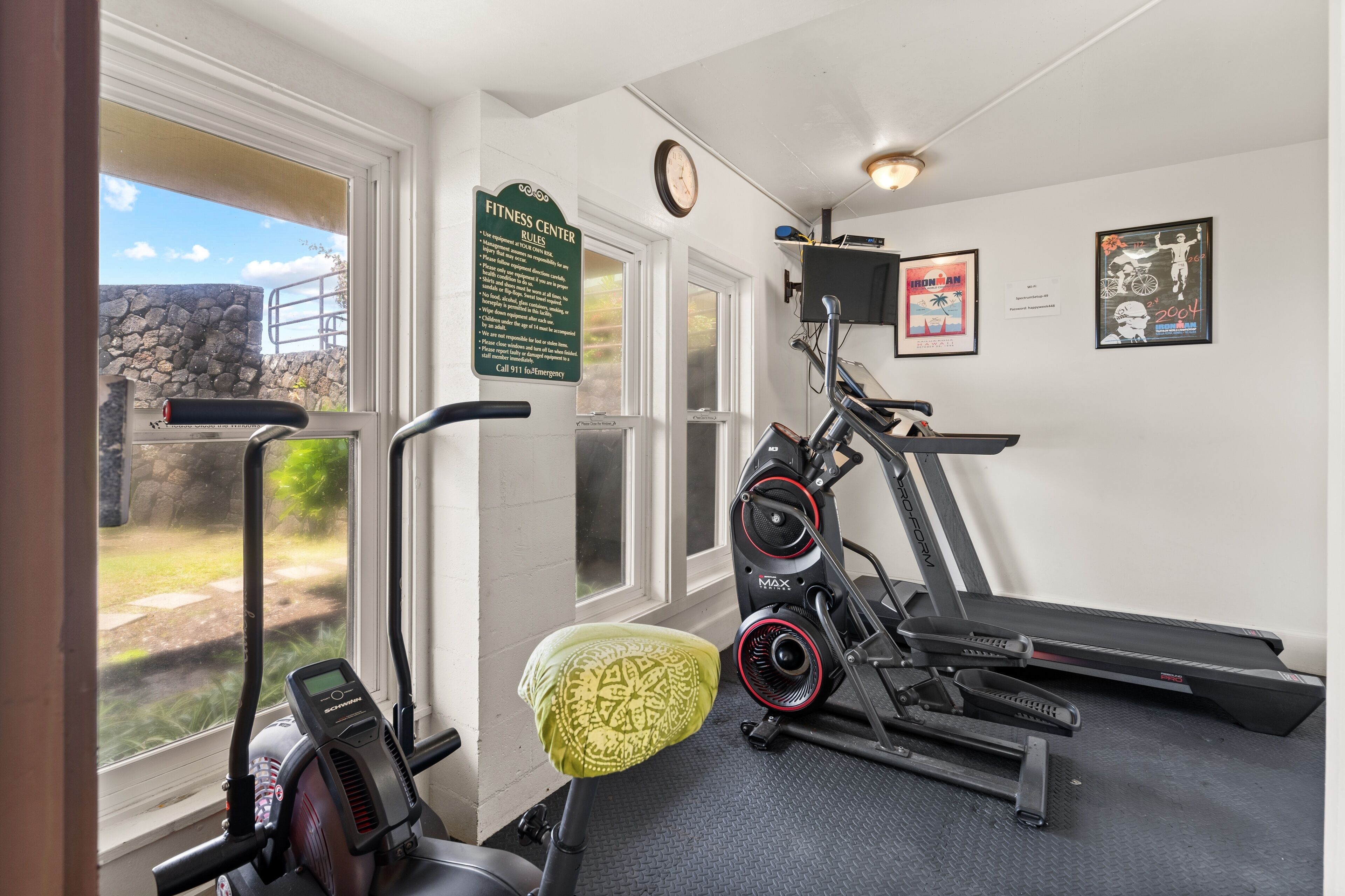 A gym with cardio equipment, a wall-mounted clock, and a sign with fitness rules.